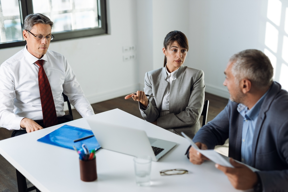 UK Workplace Etiquette Mistakes That Could Cost You: Business people talking to each other while having a business meeting in the office. 