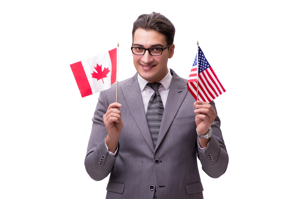 Working in Canada vs Working in the US: Picture of a business man holding a Canada and US flag